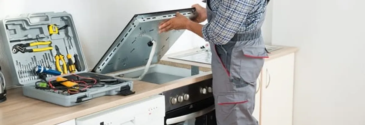 Cooktop repair technician lifting a built-in stovetop for service in Sarasota, FL