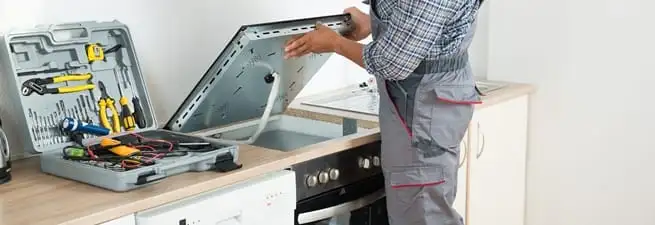 Cooktop repair technician lifting a built-in stovetop for service in Sarasota, FL