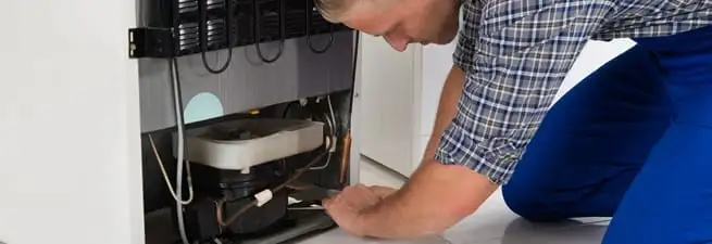 Refrigerator repair technician servicing the compressor and condenser area in Sarasota, FL