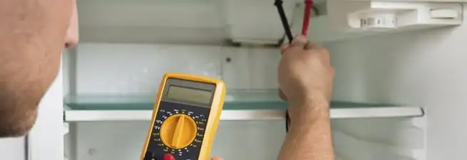 Refrigerator repair technician testing electrical components with a multimeter in Sarasota, FL